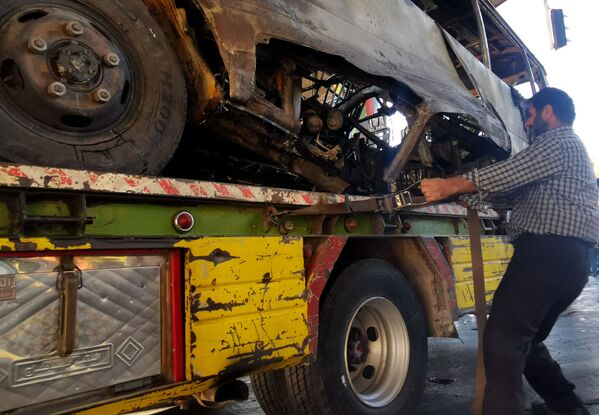 Un muncitor municipal sirian a îndepărtat autobuzul carbonizat de la locul în care a avut loc un atac cu bombă, 20 octombrie 2021. - Sputnik Moldova-România