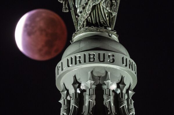 Luna, cu o eclipsă parțială de lună, este văzută în spatele scrisului „E Pluribus Unum”, traducerea din latină fiind „Din multe, unul” aflată pe Statuia Libertății din vârful cupolei de pe Capitol Hill din Washington, DC, la începutul zilei de 19 noiembrie, 2021.Cea mai lungă eclipsă parțială de Lună din ultimii 500 de ani, care va scălda Luna într-un roșu, a fost vizibilă pentru o marea majoritate a mapamondului. În timpul spectacolului ceresc se vede discul lunar aruncat aproape complet în umbră în timp ce se deplasează în spatele Pământului, înroșind 99% din față. - Sputnik Moldova-România
