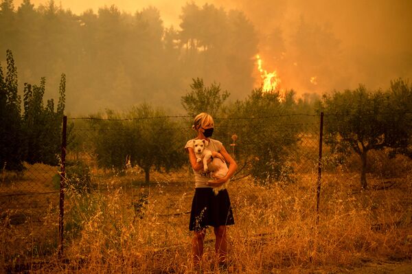 O femeie ține un câine în brațe în timp ce incendiile de pădure se apropie de satul Pefki de pe insula Evia (Eubea), a doua insulă ca mărime din Grecia, 8 august 2021. - Sputnik Moldova-România