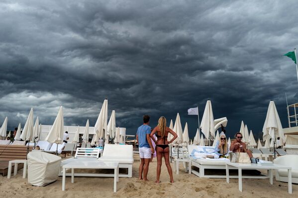 Oamenii privesc norii întunecați în timp ce stau pe o plajă din Ramatuelle, lângă Saint-Tropez, sudul Franței, pe 24 august 2021. - Sputnik Moldova-România