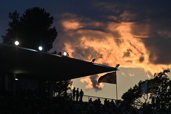 Spectatorii sunt văzuți în siluetă în tribune, în timp ce norii sunt iluminați de apusul soarelui în timpul întâlnirii de atletism IAAF Diamond League „Athletissima” de la Lausanne, pe 26 august 2021. - Sputnik Moldova-România