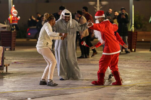 Oameni, inclusiv un bărbat îmbrăcat într-un costum de Moș Crăciun, dansează în timp ce sărbătoresc sosirea Anul Nou în Basra, Irak, vineri, 31 decembrie 2021. - Sputnik Moldova-România