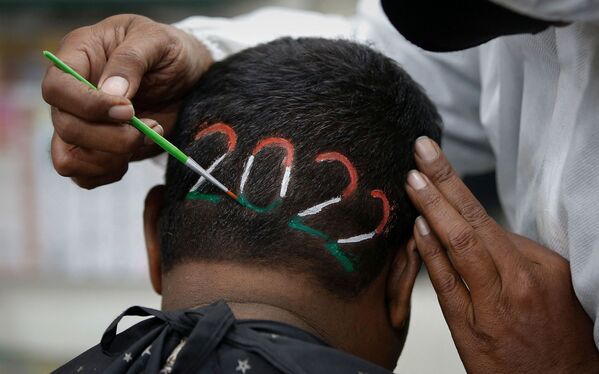 Un frizer colorează cifrele numărului 2022 după ce a tuns părul unui bărbat pentru a întâmpina noul an care vine, la o frizerie din Ahmedabad, India, 31 decembrie 2021. - Sputnik Moldova-România