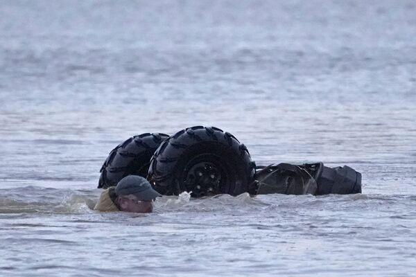 Мужчина плывет рядом со своим перевернутым вездеходом после того, как его снесло в воду. - Sputnik Молдова