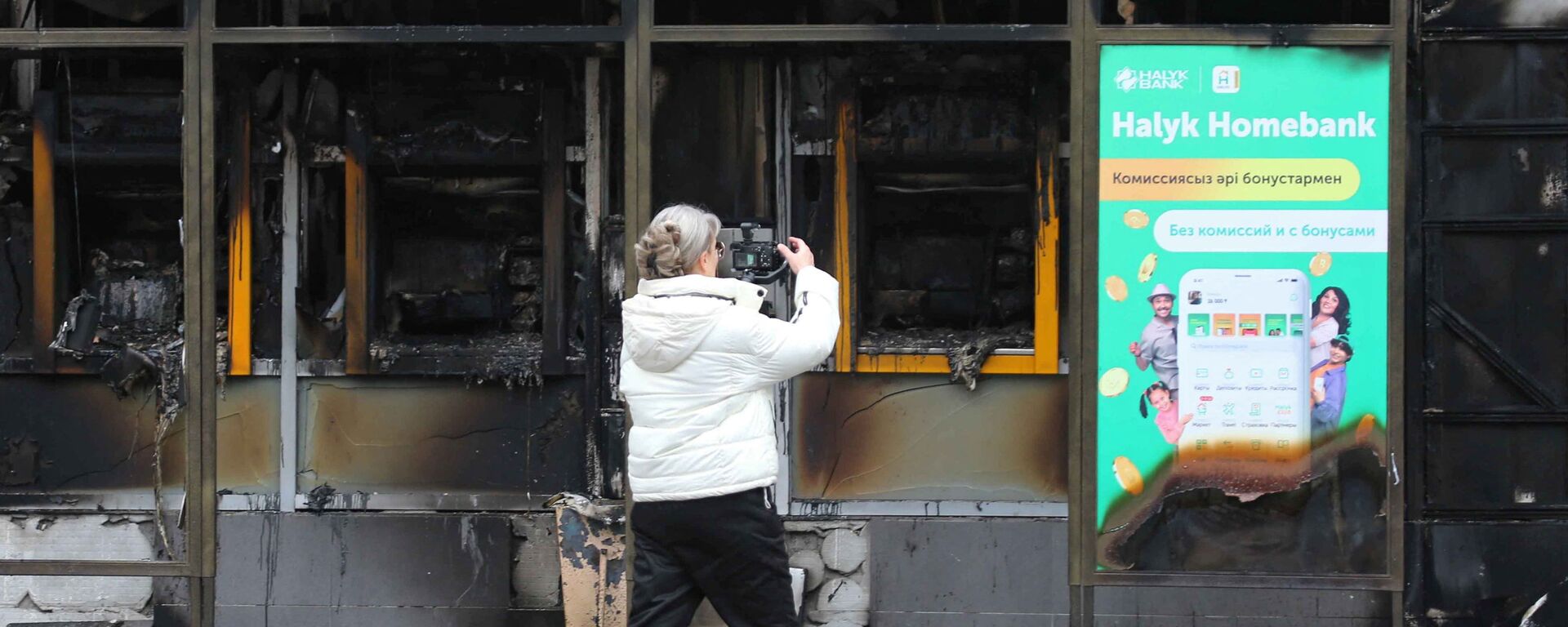 Женщина фотографирует здание, сожженное во время беспорядков в Алматы - Sputnik Молдова, 1920, 12.01.2022