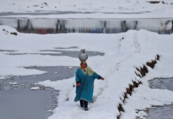 Женщина несёт воду в кувшине на голове среди заснеженного поля на окраине индийского города Сринагар. - Sputnik Молдова