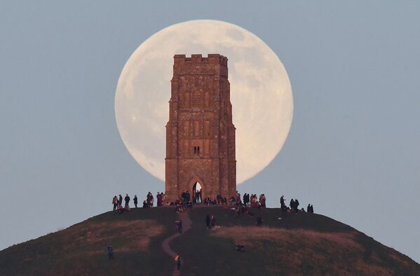 Люди стоят рядом с Башней Святого Михаила, наблюдая, как полная луна, иногда известная как &quot;Волчья луна&quot;, восходит за Гластонбери-Тор в Гластонбери, Великобритания. - Sputnik Молдова