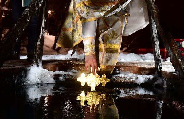 Каждому крещенскому купанию, как правило, предшествует освящение воды. На фото – священнослужитель окунает распятие в купель. - Sputnik Молдова