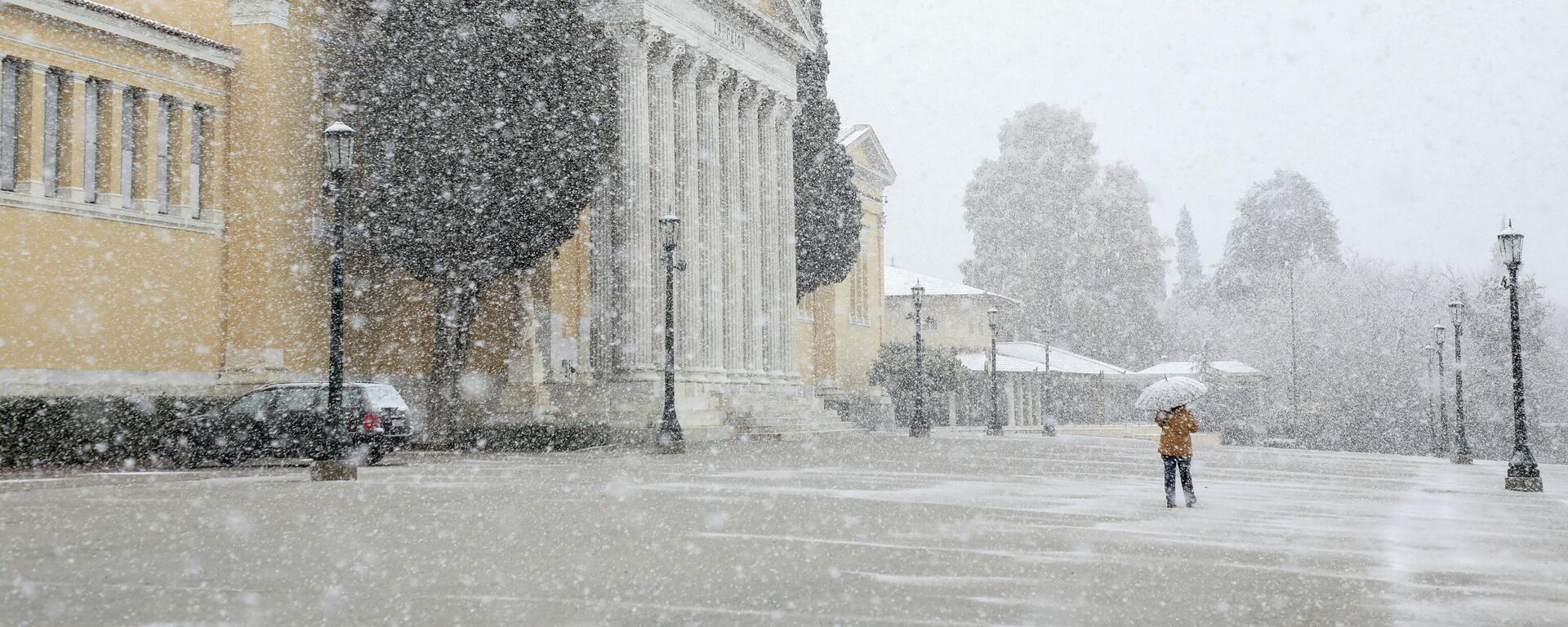 Женщина с зонтиком проходит мимо зала Заппейон во время сильного снегопада в Афинах, Греция, 24 января 2022 года. - Sputnik Молдова, 1920, 24.01.2022