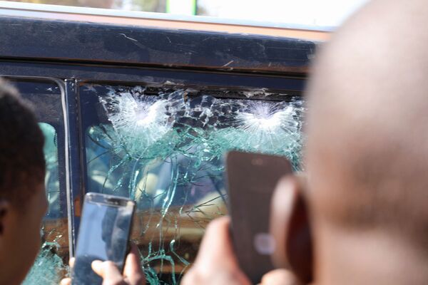 Oamenii fac fotografii la geamul unei mașini care a fost spart de gloanțe. Mașina se presupune că aparține președintelui Roch Kabore care a fost reținut într-o tabără militară din orașul Ouagadougou. Imaginile au fost surprinse la 24 ianuarie în Burkina Faso.  - Sputnik Moldova