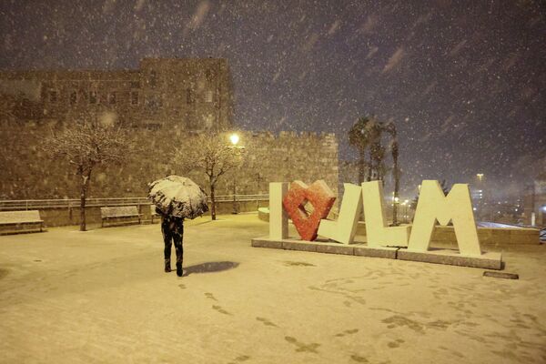 Мужчина прикрывается зонтиком во время снежной бури в Иерусалиме. - Sputnik Молдова