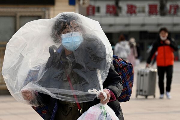 Женщина, прикрывающаяся пластиковым пакетом, возле железнодорожного вокзала в Пекине. - Sputnik Молдова