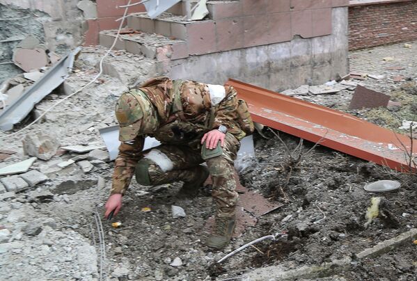 Un militar inspectează un crater de la o explozie în curtea unei clădiri rezidențiale cu mai multe etaje din Donețk, avariat de bombardamente. - Sputnik Moldova-România