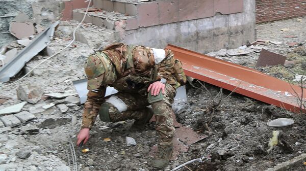 Военнослужащий обследует воронку от взрыва во дворе многоэтажного жилого дома в Донецке, поврежденного в результате обстрела - Sputnik Молдова