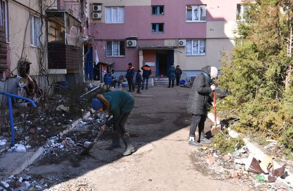 Localnicii curăță gunoiul în curtea unei clădiri de locuit, avariate de bombardamente în Volnovaha. - Sputnik Moldova