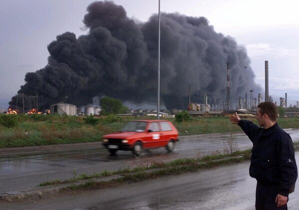 Un angajat din serviciile de securitate arată spre un incendiu la rezervoarele rafinăriei de petrol din Pancevo, la aproximativ 16 km (10 mile) nord de Belgrad, duminică, 18 aprilie 1999.  - Sputnik Moldova-România