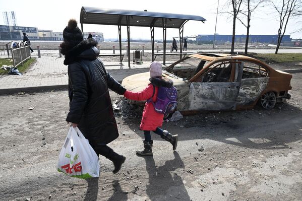 O femeie cu un copil de mână trec pe lângă o mașină distrusă, în Mariupol - Sputnik Moldova