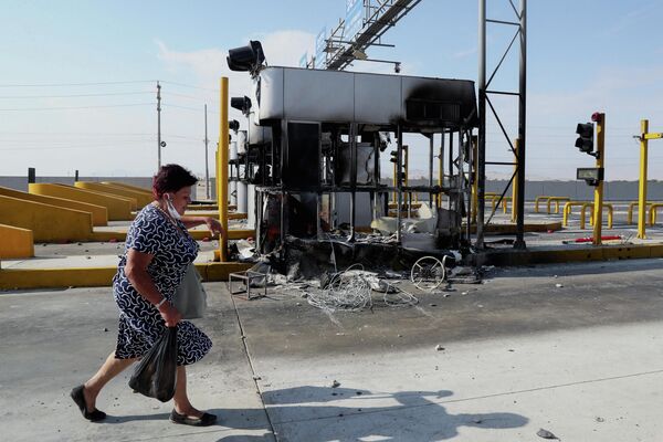 O femeie trece pe lângă cabinele de taxare arse pe o autostradă care duce spre Lima în timpul grevei naționale a transporturilor împotriva prețurilor la gaz și a taxelor de drum, în Ica, Peru, 4 aprilie 2022. - Sputnik Moldova