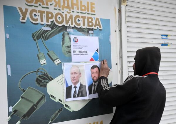 Un bărbat lipește portretele președintelui Rusiei, Vladimir Putin, și cel al Republicii Populare Donețk, Denis Pușilin, în preajma centrului de ajutor umanitar din sectorul Levoberejie al Mariupolului. - Sputnik Moldova