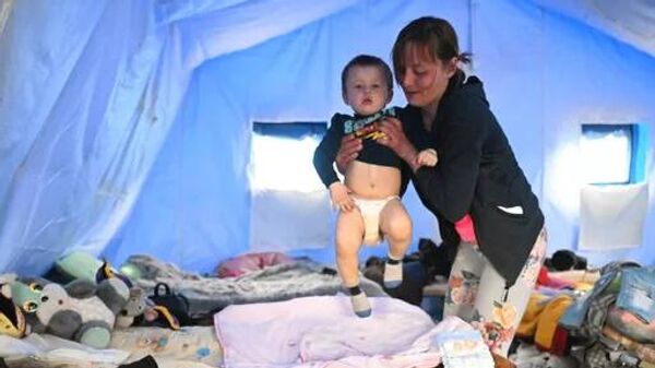 O femeie cu un copil într-un cort pe teritoriul centrului de cazare temporară pentru evacuați din Mariupol - Sputnik Moldova-România