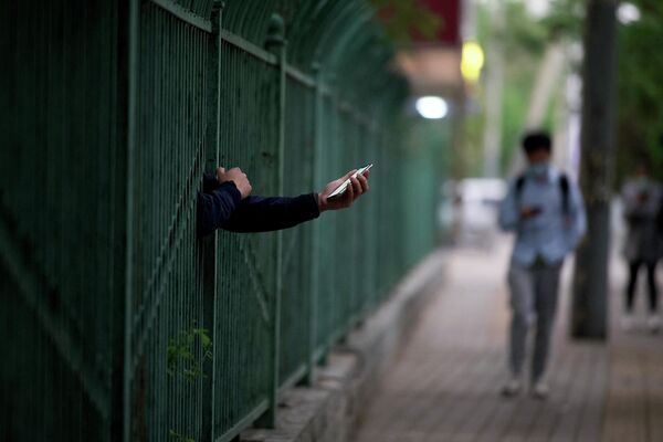 Человек протягивает руку с мобильным телефоном через забор жилого района, находящегося на локдауне в Пекине, Китай. - Sputnik Молдова