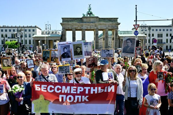 Oamenii ridică portrete ale soldaților sovietici și țin un banner pe care scrie „Regimentul Nemuritor” în timp ce mărșăluiesc de la Poarta Brandenburg la Memorialul de Război Sovietic din Tiergarten din Berlin, pe 9 mai 2022 - Sputnik Moldova-România