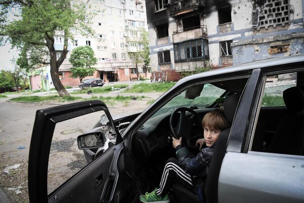 Дети играют в разбитой машине возле одного из домов в Мариуполе - Sputnik Молдова