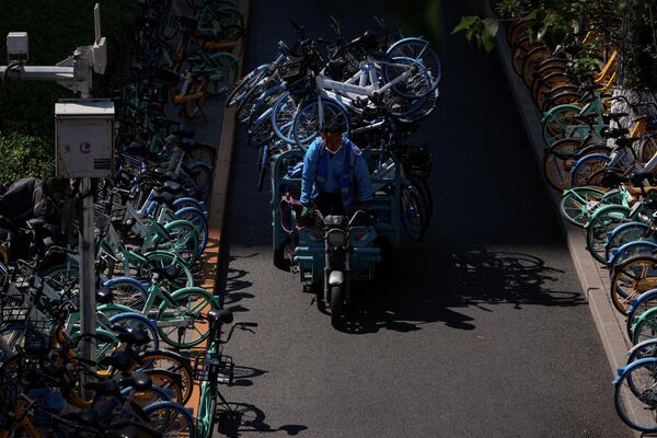 Рабочий едет на тележке с общими велосипедами мимо рядов неиспользуемых общих велосипедов, припаркованных вдоль улицы в районе Чаоян в утренний час пик, поскольку большинству сотрудников было приказано работать из дома в понедельник, 16 мая, в Пекине.  - Sputnik Молдова