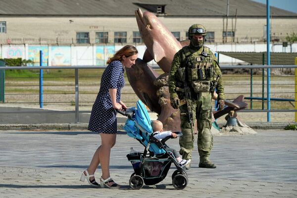 O femeie cu copilul trece pe lângă un soldat rus. Imaginea a fost surprinsă în regiunea Herson, vineri, 20 mai 2022. Această fotografie a fost făcută în timpul unei călătorii organizate de Ministerul rus al Apărării - Sputnik Moldova