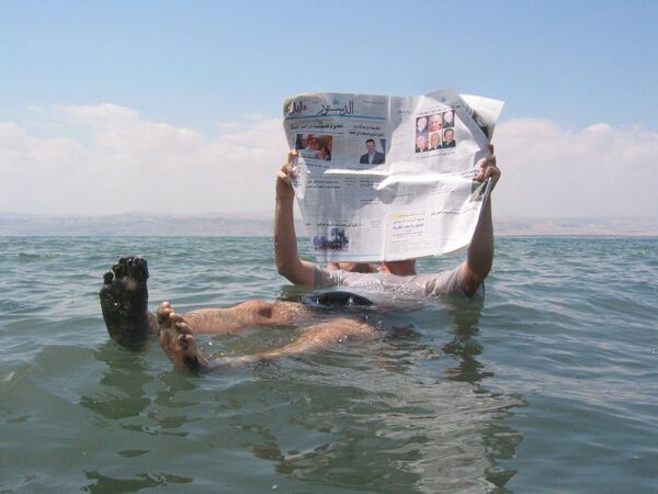 Человек лежит с газетой на поверхности Мёртвого моря, самого соленого водоема на Земле - Sputnik Молдова