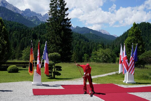 Un muncitor curăță covorul roșu aflat pe teritoriul Castelul Elmau, iar  pe fundal pot fi observaţi munții bavarez, 26 iunie 2022 - Sputnik Moldova-România