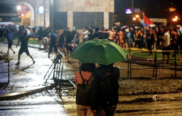 Пара под зонтиком наблюдает, как люди бросают камни в полицию и здание парламента. - Sputnik Молдова
