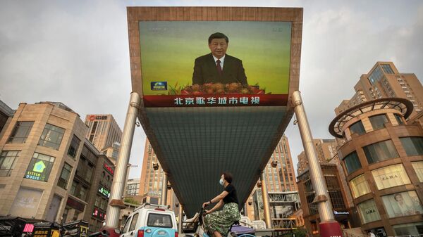 Женщина в маске проезжает на велосипеде мимо большого телевизионного экрана в торговом центре, где транслируется репортаж китайского телевидения о визите президента Китая Си Цзиньпина в Гонконг в Пекине - Sputnik Moldova-România