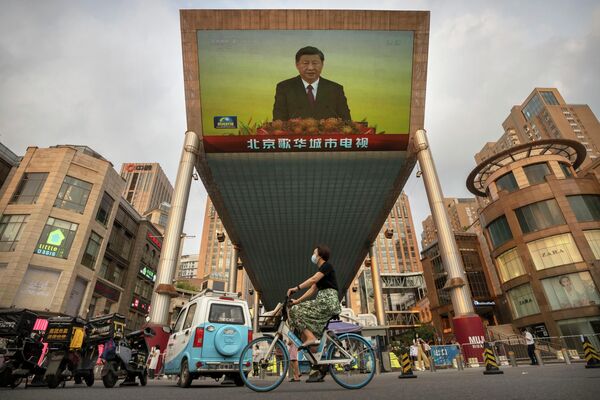 Женщина в маске проезжает на велосипеде мимо большого телевизионного экрана в торговом центре, где транслируется репортаж китайского телевидения о визите президента Китая Си Цзиньпина в Гонконг в Пекине. - Sputnik Молдова