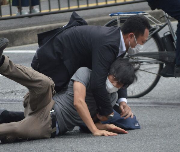 Un bărbat (jos) suspectat că l-a împușcat pe fostul premier japonez Shinzo Abe este culcat și imobilizat la pământ de poliție în stația Yamato Saidaiji din orașul Nara, pe 8 iulie 2022. - Sputnik Moldova