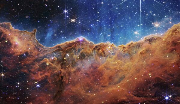 На этом изображении, опубликованном НАСА 12 июля 2022 года с космического телескопа Джеймса Уэбба (JWST), показан пейзаж из &quot;гор&quot; и &quot;долин&quot;, усеянных сверкающими звездами, который на самом деле является краем соседней молодой области звездообразования  NGC 3324 в туманности Киля. - Sputnik Молдова
