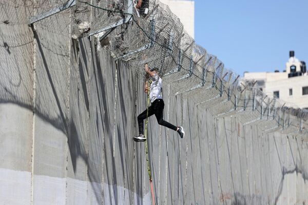 Юноша спускается по веревке через бетонную стену вызывающего споры израильского разделительного барьера в районе Бейт-Ханина в Восточном Иерусалиме после того, как поднялся и перебрался из деревни аль-Рам, 11 июля 2022 года. - Sputnik Молдова