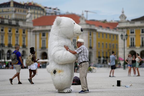 Мужчина разговаривает с человеком в костюме белого медведя на площади Комерсио в Лиссабоне, понедельник, 11 июля 2022 года. За последние пару дней температура в Португалии снизилась, что принесло некоторую передышку от аномальной жары, но ожидается, что  она снова поднимется и достигнет 46 градусов Цельсия. - Sputnik Молдова