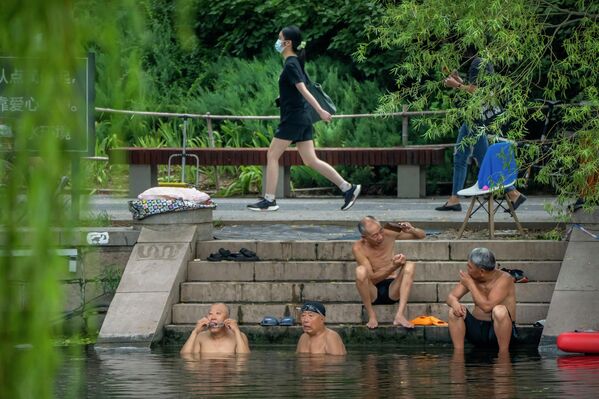 Жара в Пекине: женщина в маске проходит мимо мужчин, купающихся в водоеме. - Sputnik Молдова