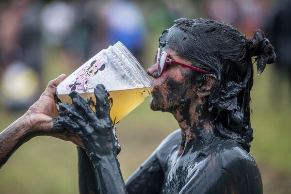 Un petrecăreț bea bere în timpul festivalului „Bloco da Lama”, este o petrecere de carnaval cu noroi, în Paraty, statul Rio de Janeiro, Brazilia, pe 22 februarie 2020.  - Sputnik Moldova-România