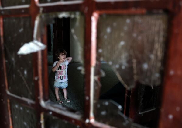 Un copil palestinian stă în spatele unei ferestre sparte în interiorul unei clădiri avariate în urma atacurilor aeriene israeliene de la Rafah, în sudul Fâșiei Gaza, pe 7 august 2022. - Sputnik Moldova-România