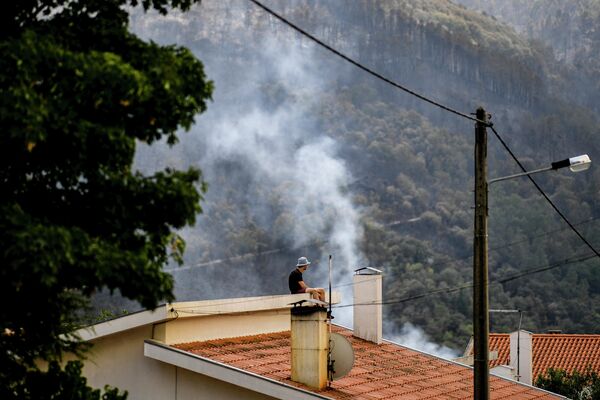 Un bărbat urmărește extinderea unui incendiu de pădure de pe acoperișul unei case din satul Sameiro, lângă orașul Manteigas, pe 10 august 2022. - Un incendiu care a izbucnit sâmbătă a făcut ravagii în parcul natural Serra da Estrela în centrul Portugaliei. - Sputnik Moldova-România