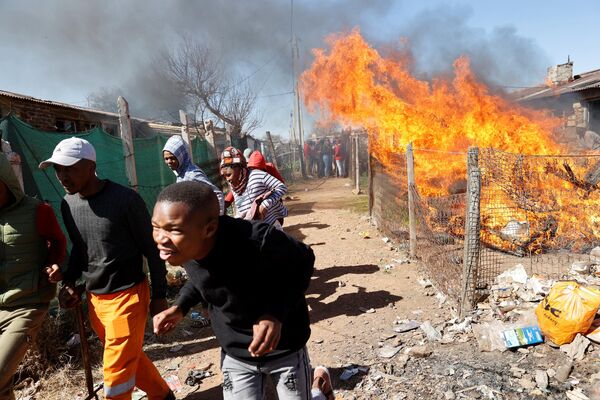 Члены общины Мохленкен убегают от пожара, в котором горят вещи шахтеров, работающих нелегально, во время демонстрации против незаконной добычи полезных ископаемых, ЮАР - Sputnik Молдова