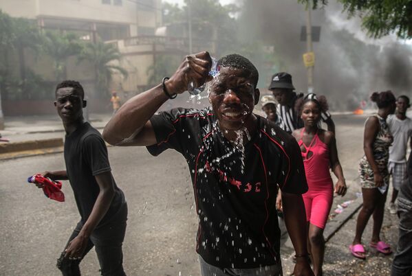 Протестующий, пострадавший от слезоточивого газа, выпущенного полицией, брызгает водой на лицо во время акции протеста с требованием улучшения качества жизни в Порт-о-Пренс, Гаити. - Sputnik Молдова