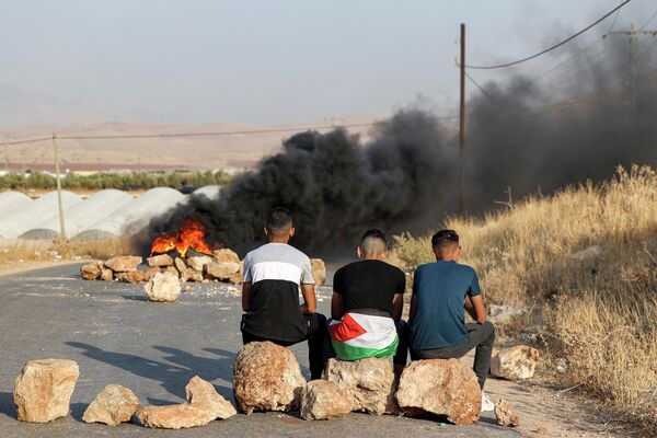 Палестинские мужчины сидят на камнях возле горящих шин, протестуя против закрытия дороги рядом с местом нападения на израильский автобус к востоку от палестинского города Тубас - Sputnik Молдова