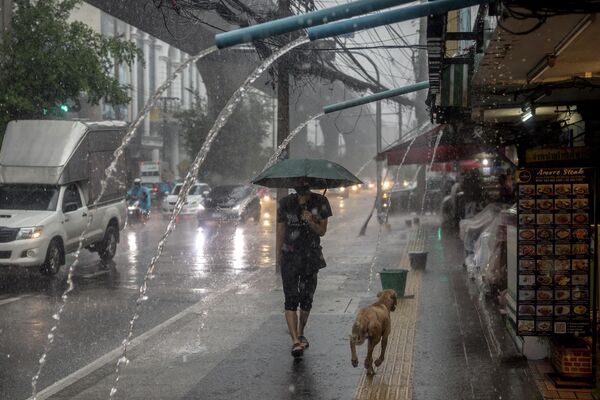 Мужчина на улице во время сильного дождя в Бангкоке. - Sputnik Молдова