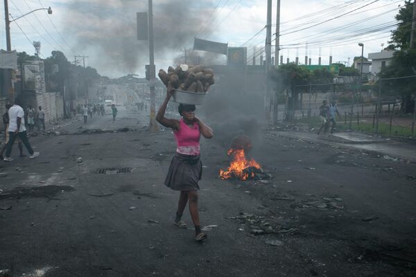 Уличный торговец проходит мимо баррикады, воздвигнутой демонстрантами в знак протеста против повышения цен на топливо и с требованием отставки премьер-министра Гаити Ариэля Генри в Порт-о-Пренсе, Гаити, в понедельник, 19 сентября 2022 года. - Sputnik Молдова