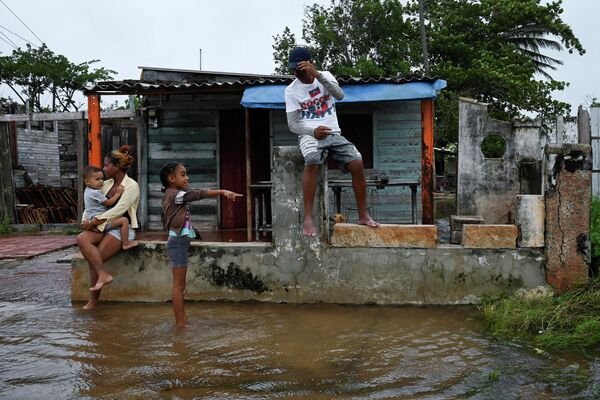 O familie observată în afara casei lor inundate din Batabano, Cuba, pe 27 septembrie 2022, în timpul trecerii uraganului Ian. Uraganul Ian a atins pământul în vestul Cubei marți dimineața, furtuna provocând evacuări în masă și temeri că va aduce distrugeri la scară largă în timp ce se îndreaptă spre statul american Florida. (Foto de YAMIL LAGE / AFP) - Sputnik Moldova-România