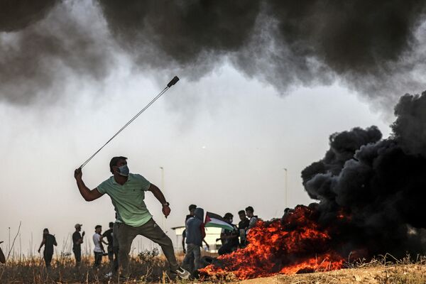 Палестинский протестующий бросает камни на границе с Израилем в районе города Газа - Sputnik Молдова