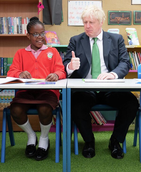 Ex-premierul Marii Britanii, Boris Johnson, face un gest cu „degetul mare” în timp ce stă în bancă alături de elevii de la Academia Primară St Mary Cray din sud-estul Londrei, 23 mai 2022. - Sputnik Moldova-România